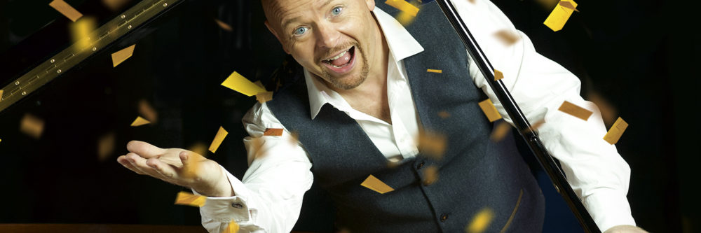 Jon Courtenay on piano surrounding by gold confetti